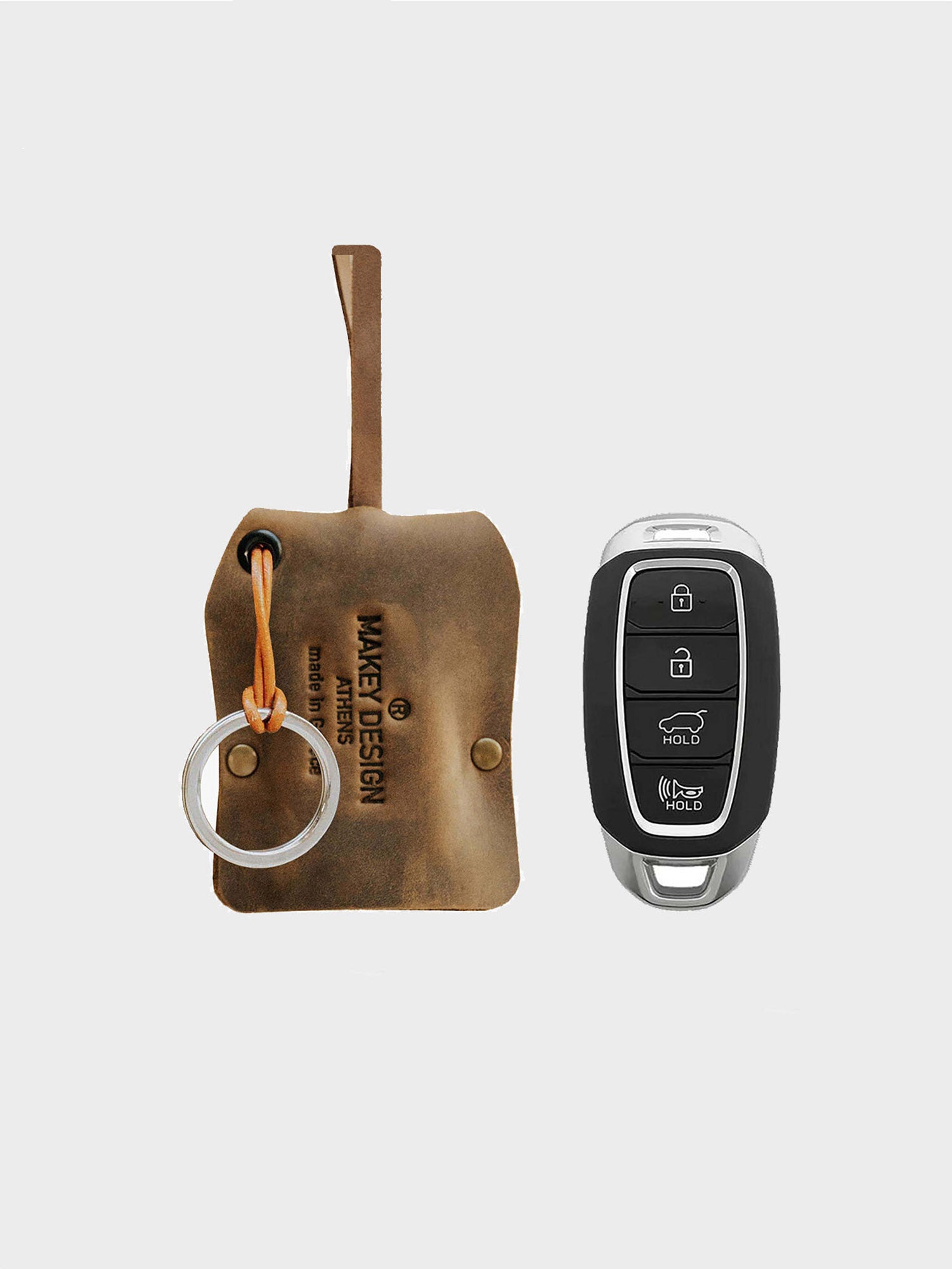 A brown leather key case with a metal keychain next to a modern car key fob.