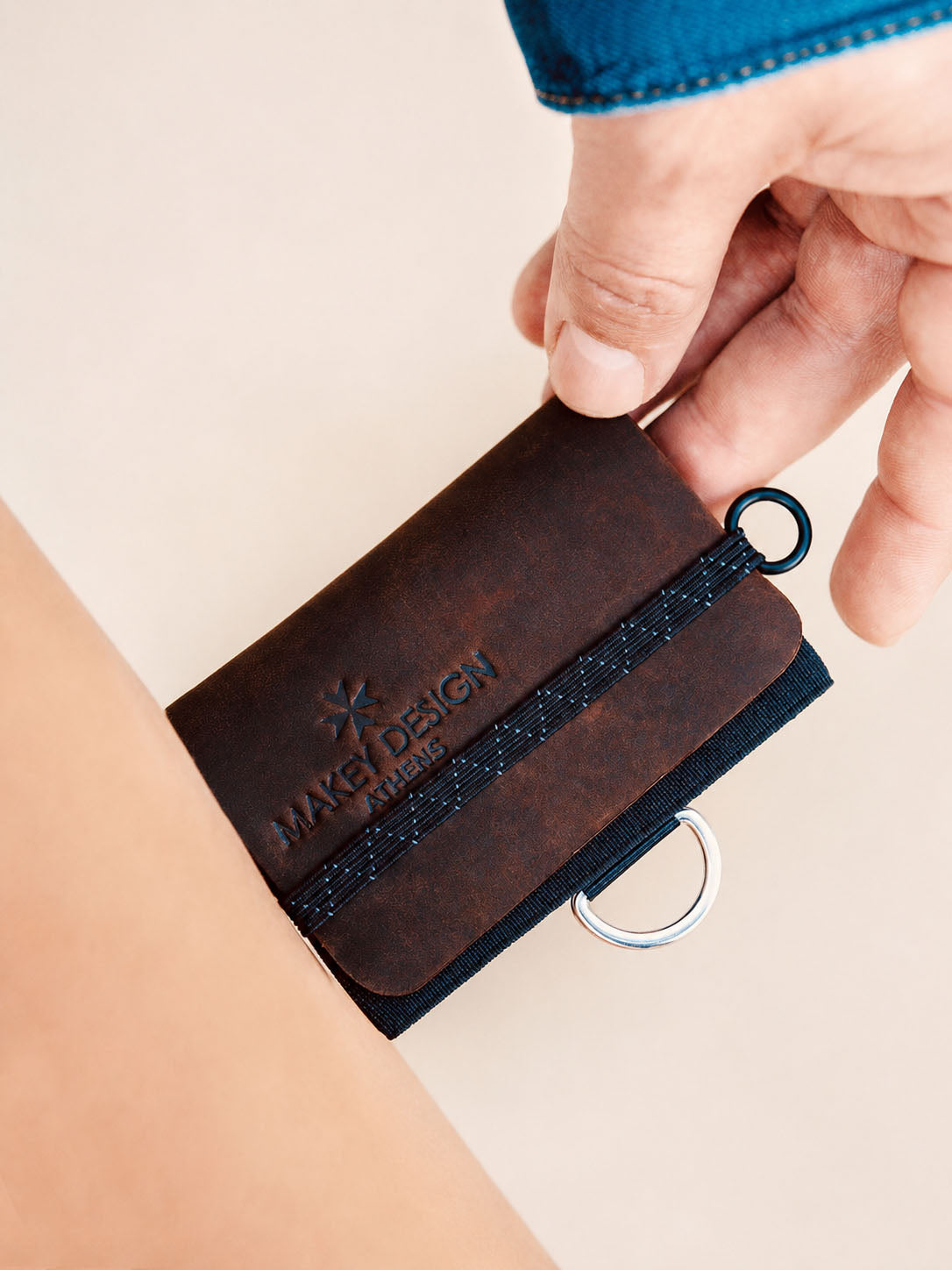 Brown leather key organizer with a ring held by a hand on a beige background