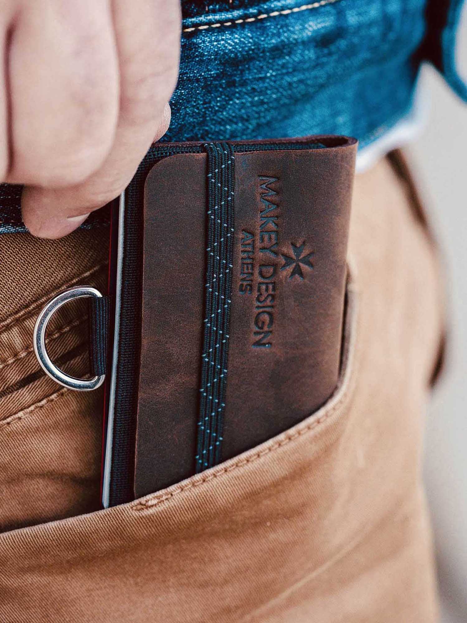 Brown leather wallet with 'MAKEY DESIGN' branding being placed into a pocket.