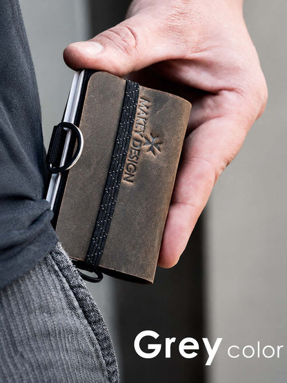 Hand holding a brown leather wallet with 'MAKEY DESIGN' branding against a gray background.